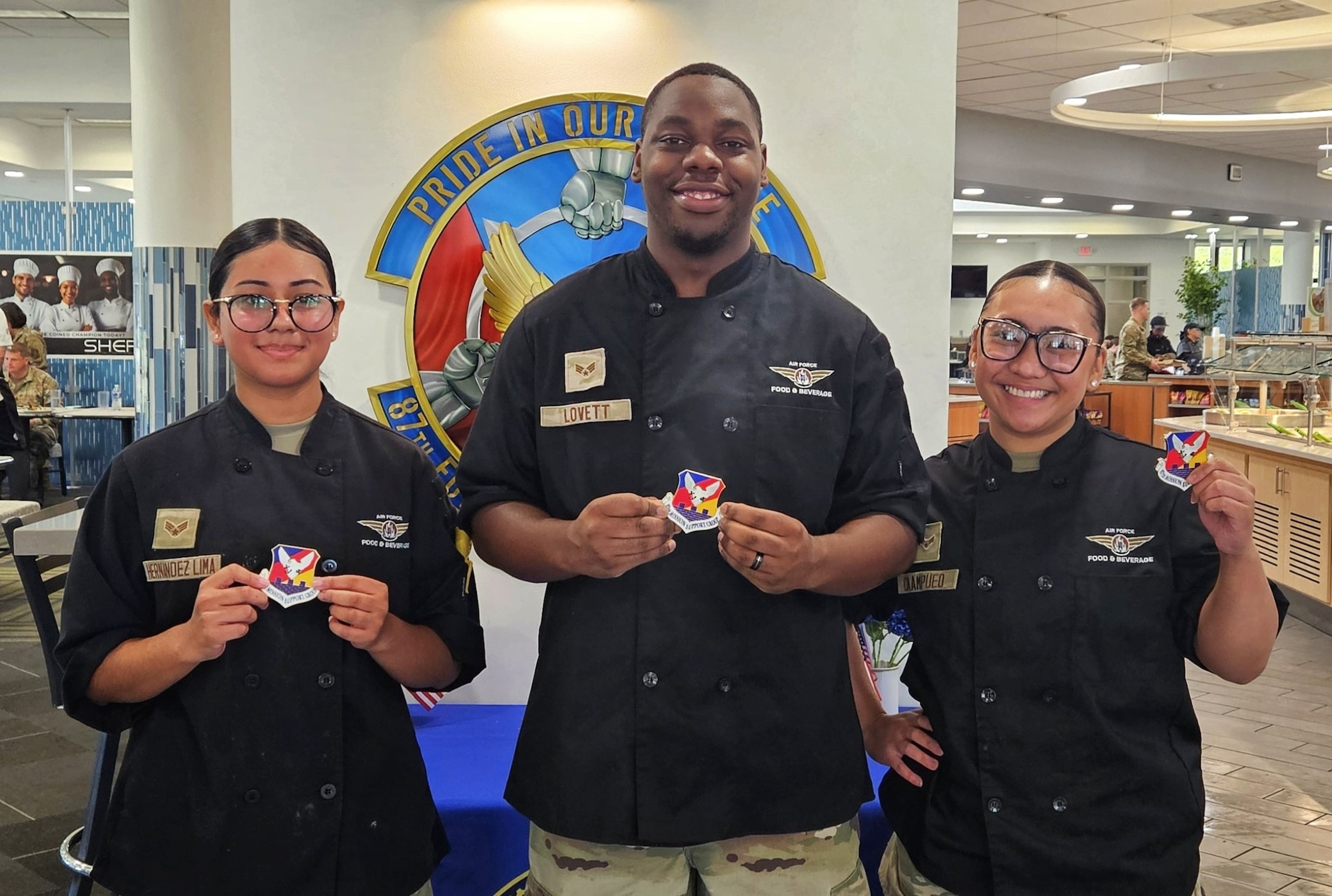 U.S. Air Force Senior Airman Nidia Hernandez-Lima (left), Senior Airman Jaylen Lovett (center) and Airman 1st Class Shanise Caampued, 87th Force Support Squadron food service specialists, show off their squadron patch after competing in the 87th FSS Salute Hospitality Epicurean Faceoff in September at Joint Base McGuire-Dix-Lakehurst, N.J. Caampued earned first place and will represent JB MDL at the national SHEF competition Dec. 3, 2025 at the Culinary Institute of America in San Antonio, Texas. (Air Force Courtesy Photo)