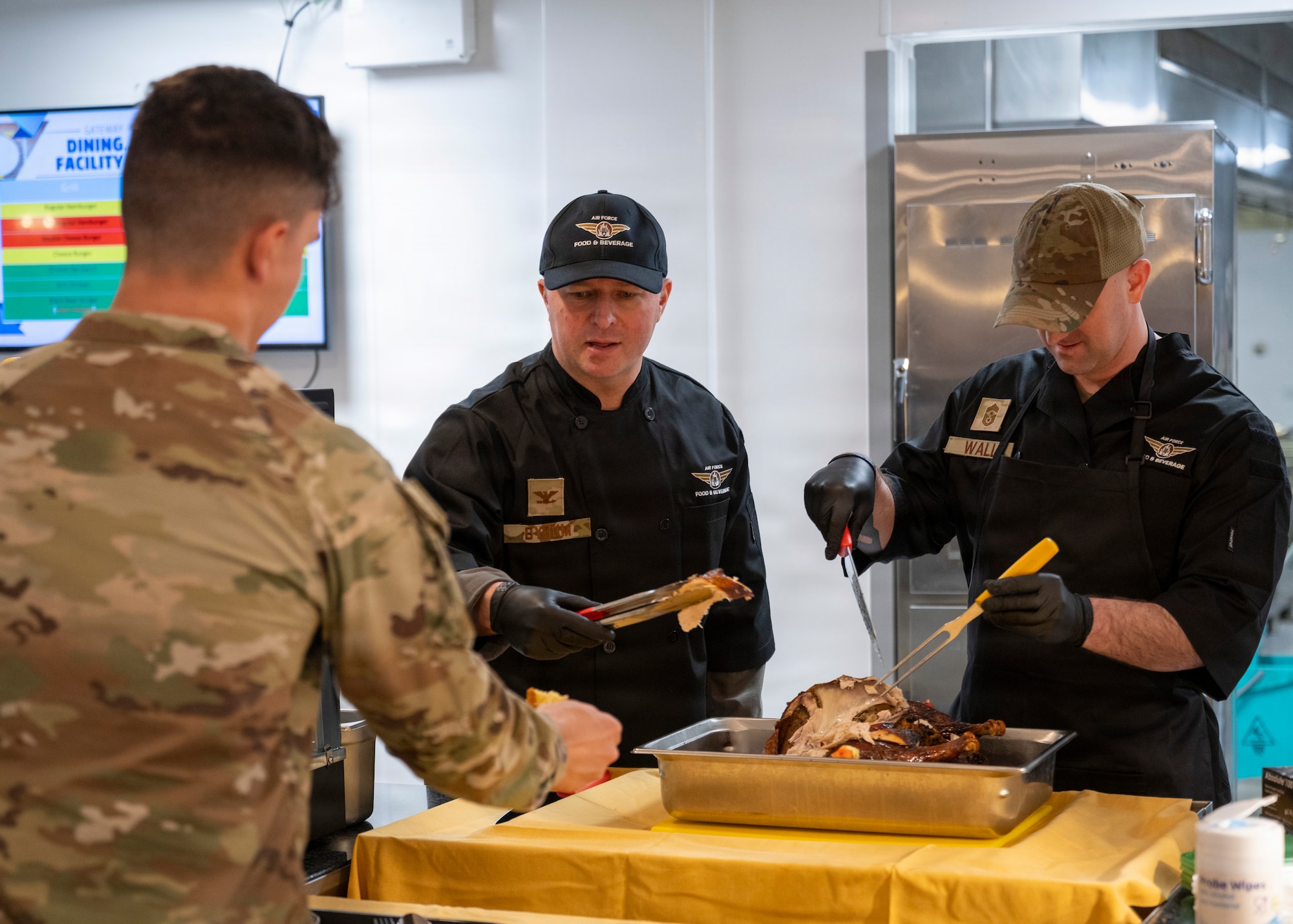Col. Steven Byrum, 100th Air Refueling Wing commander and Chief Master Sgt. James Wall, 100th ARW command chief, serve turkey to Airmen for a Thanksgiving lunch at RAF Mildenhall, Nov. 26, 2025. The 100th Force Support Squadron and base leadership prepared and served meals to Airmen who are stationed away from home this holiday season. (U.S. Air Force photo by Staff Sgt. Nash Truitt)
