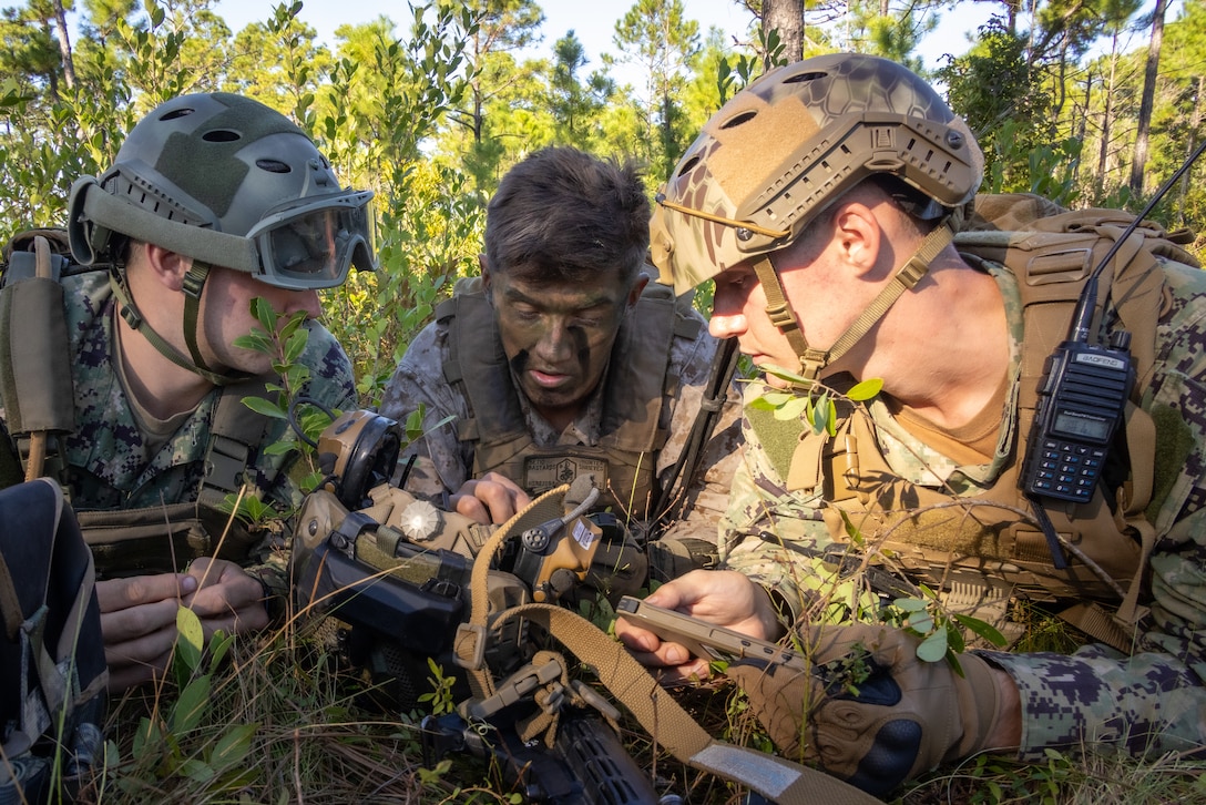 U.S. Marine Corps 1st Lt. Hunter Shrieves, center, an infantry officer with 3rd Battalion, 2nd Marine Regiment, 2nd Marine Division, center, instructs Naval Academy Midshipmen 3rd class Carter Breen, left, and Midshipmen 2nd Class Daniel Reedy, on Marine Corps operating procedures during a Marine Corps Combat Readiness Evaluation on Marine Corps Base Camp Lejeune, North Carolina, Oct. 20, 2025.