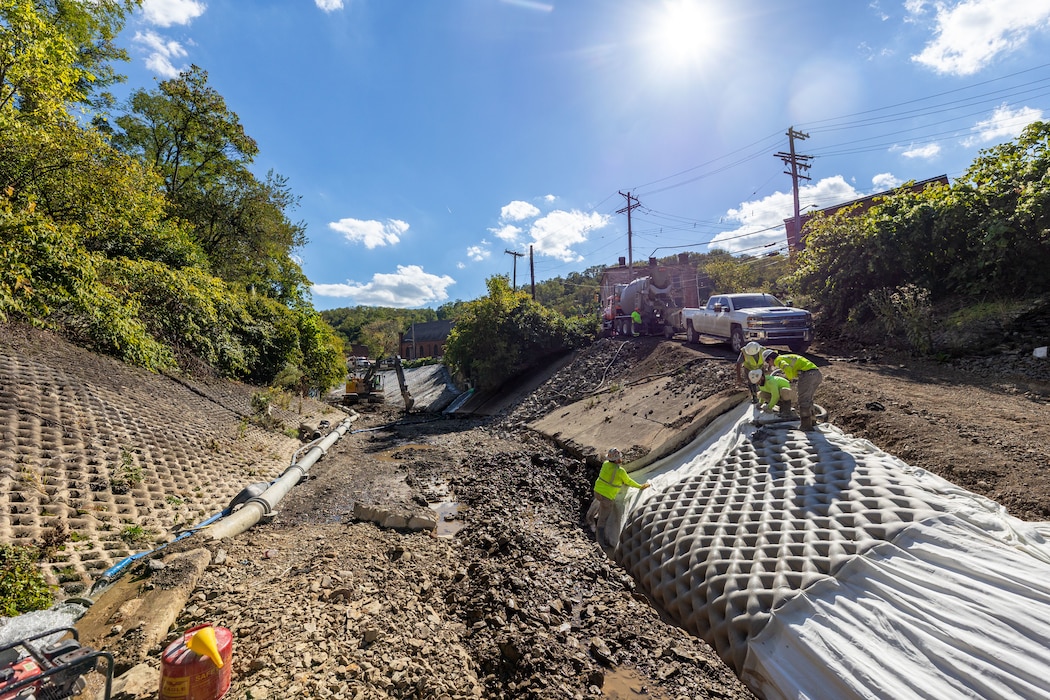 In a flood protection-project channel, construction workers stand on the channel's revetment.