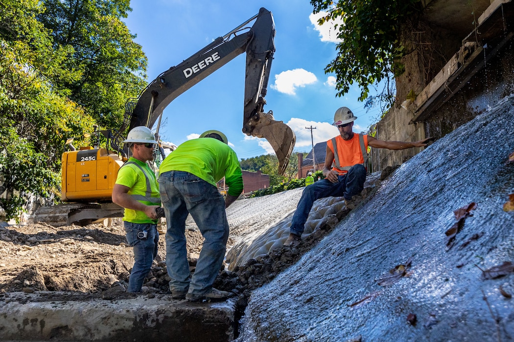 In a flood protection-project channel, a construction worker hands stone to another construction worker.