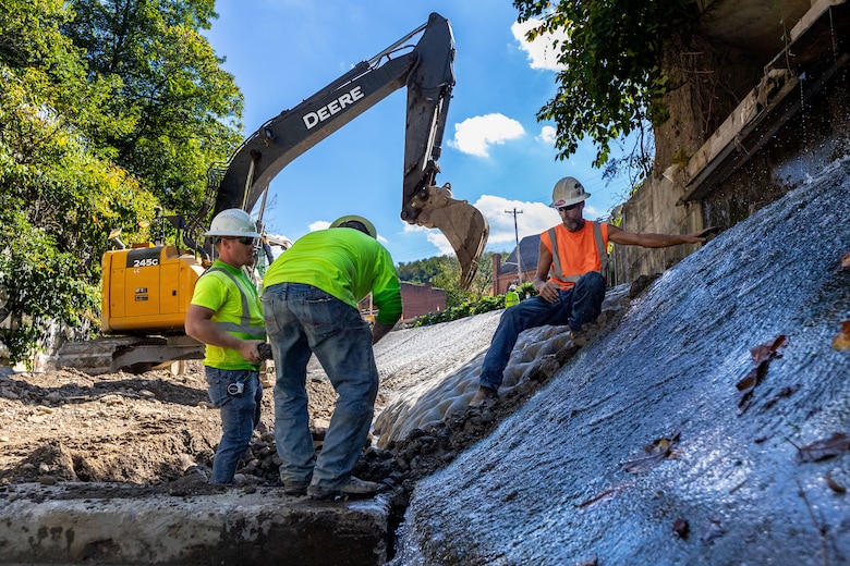In a flood protection-project channel, a construction worker hands stone to another construction worker.