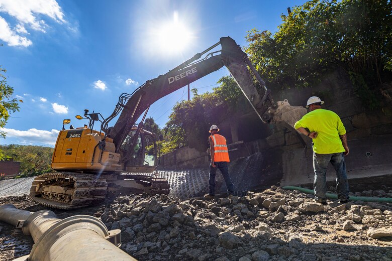 In a flood protection-project channel, construction workers stand near an excavator.