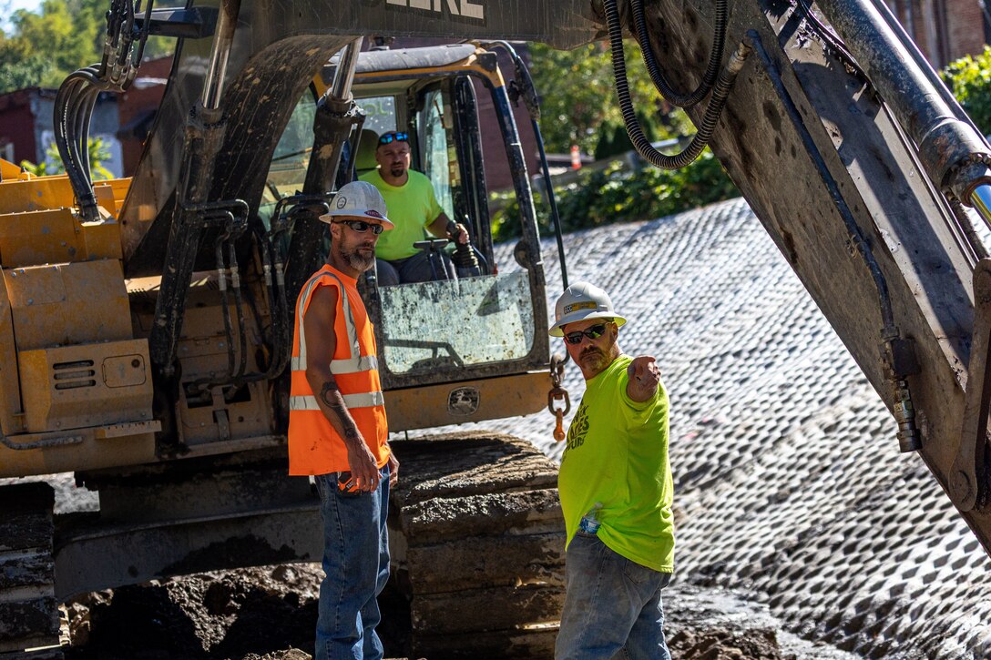 In a flood protection-project channel, construction workers stand near an excavator.