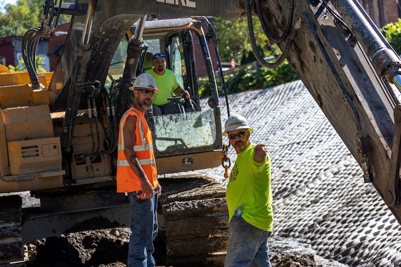 In a flood protection-project channel, construction workers stand near an excavator.