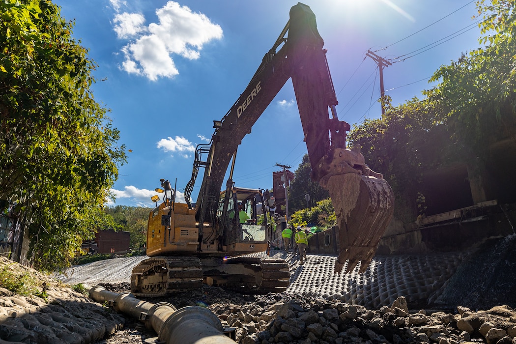 In a flood protection-project channel, a construction worker operates an excavator.