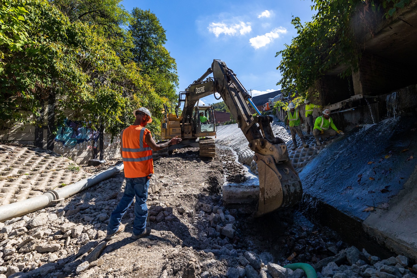 In a flood protection-project channel, construction workers stand near an excavator.