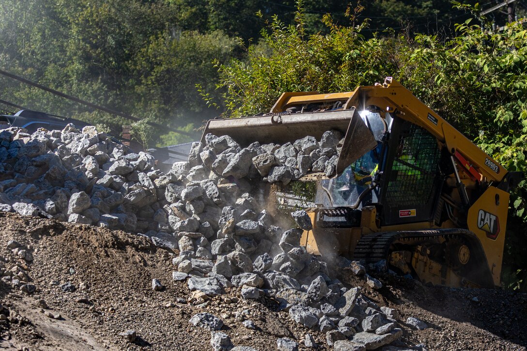 In a flood protection-project channel, a construction worker moves stone with an excavator.