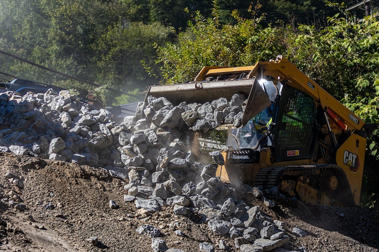 In a flood protection-project channel, a construction worker moves stone with an excavator.