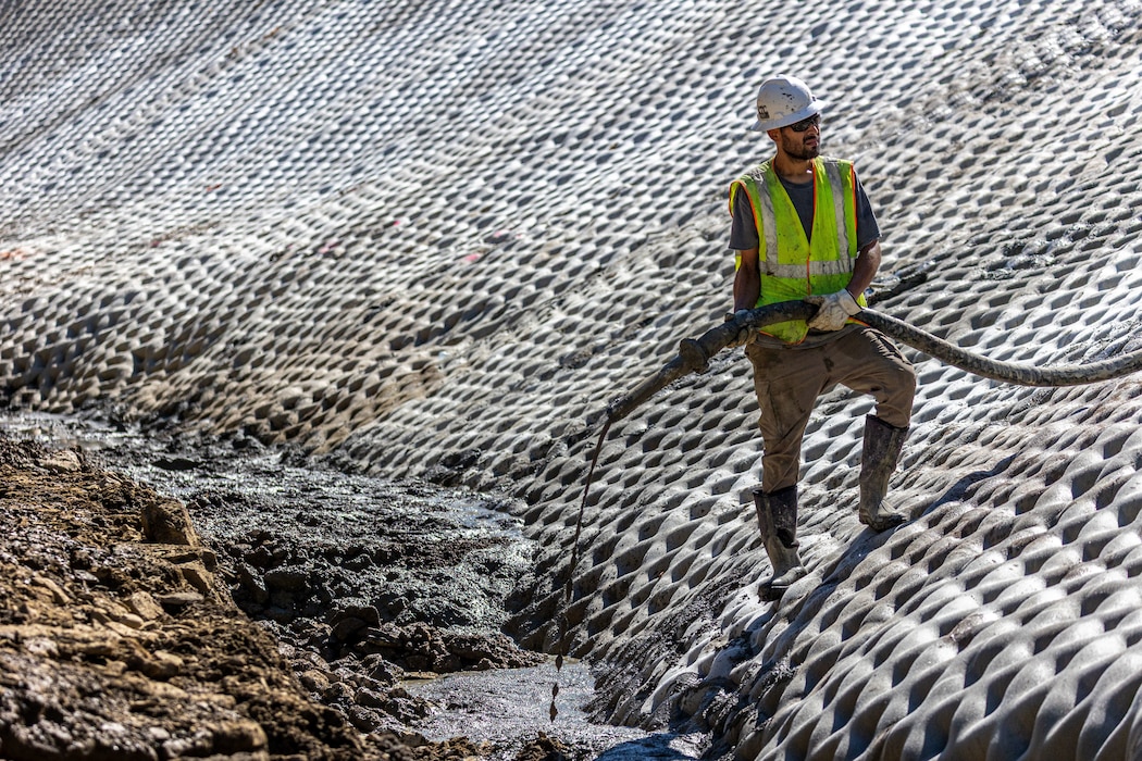 A construction worker holds a hose in a flood protection project channel.