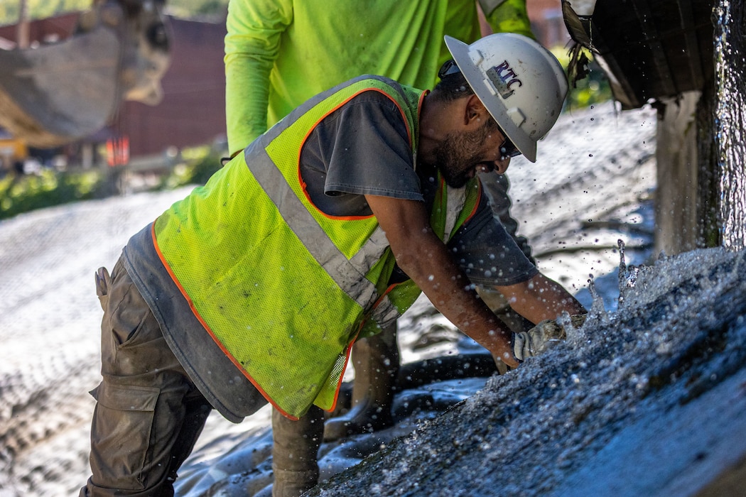 A construction worker places stone in a channel.