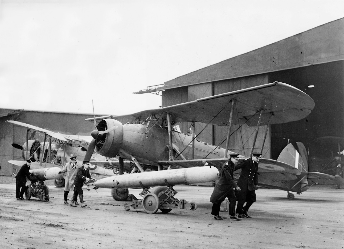 Another torpedo-loading operation shows the weapon being wheeled toward is aircraft in 1940-41, during which period, many Swordfish squadrons flew from such shore stations., usually under Royal Air Force control.