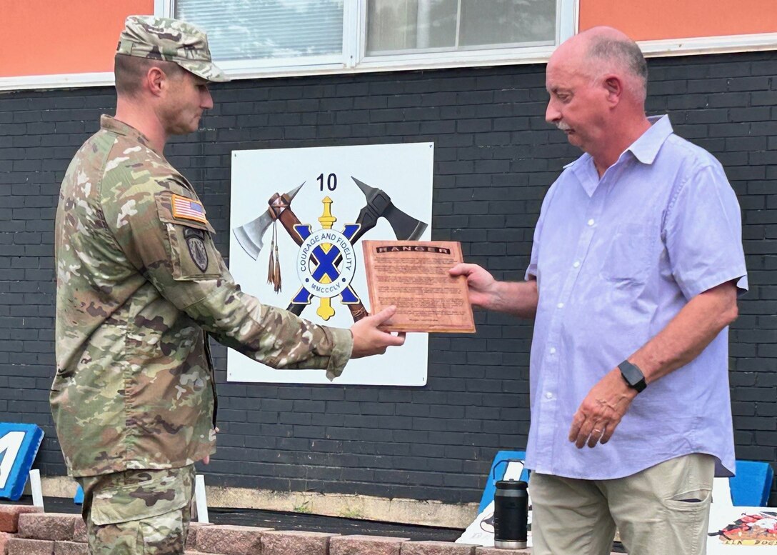 A man in an Army camouflage uniform hands a man with a blue shirt on a plaque.