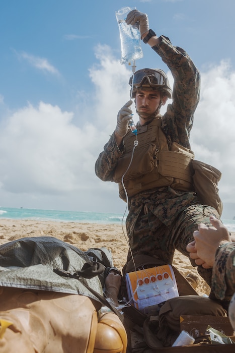 U.S. Navy Petty Officer 3rd Class, Samuel Souba, a hospital corpsman with 3rd Littoral Logistics Battalion, 3rd Marine Littoral Regiment, 3rd Marine Division, prepares fluids for a simulated casualty during a training evolution on Marine Corps Training Area Bellows, Hawaii, Nov. 12, 2025. The training enhanced medical evacuation skills using support vehicles, strengthened proficiency across evacuation methods, and integrated in-transit medical care. Souba is a native of Virginia. (U.S. Marine Corps photo by Sgt. Jonathan Beauchamp)