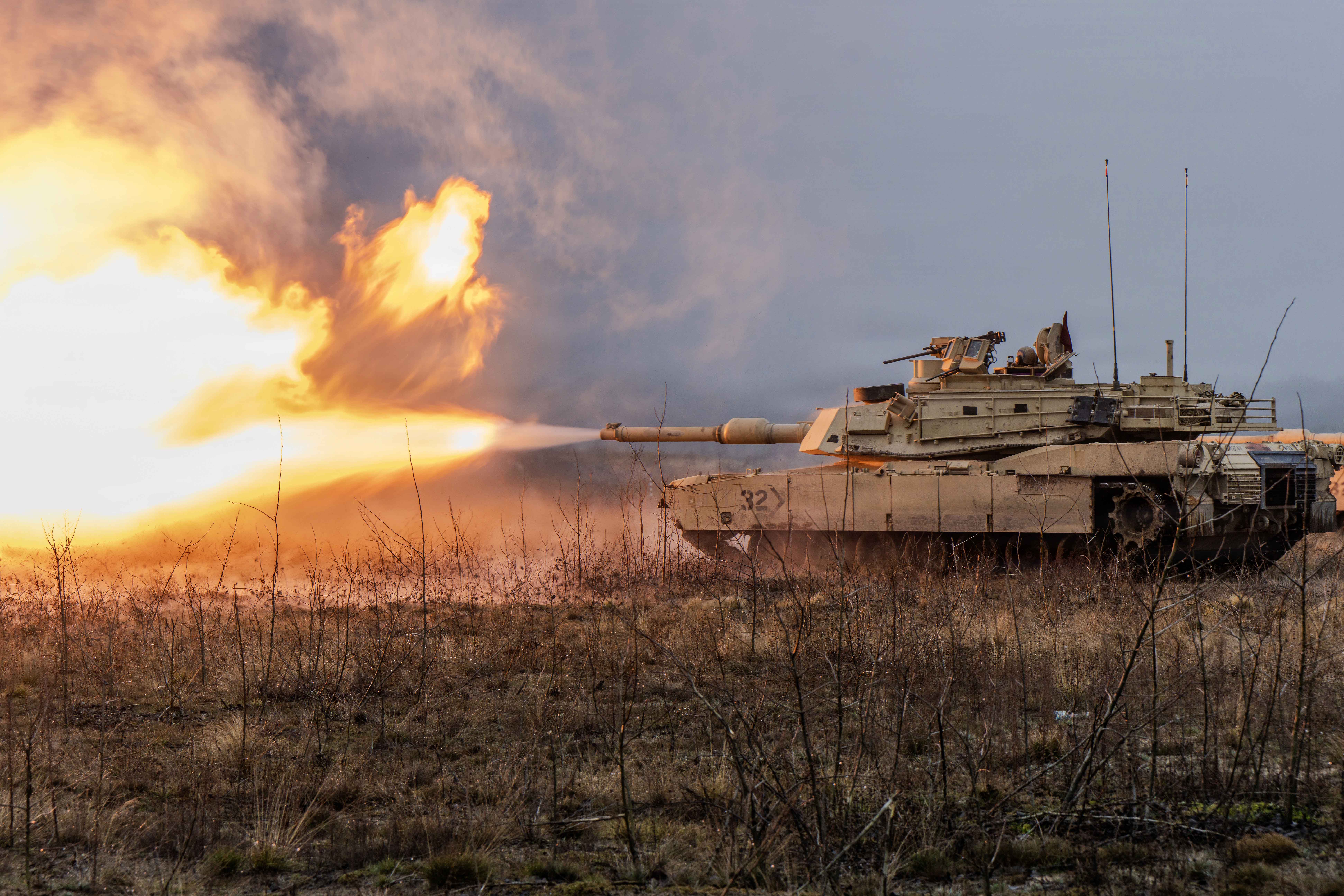 Flames and smoke shoot from the gun of a tank in a field.