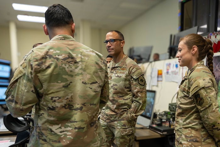 Two men and a woman in military uniforms stand in a circle talking.