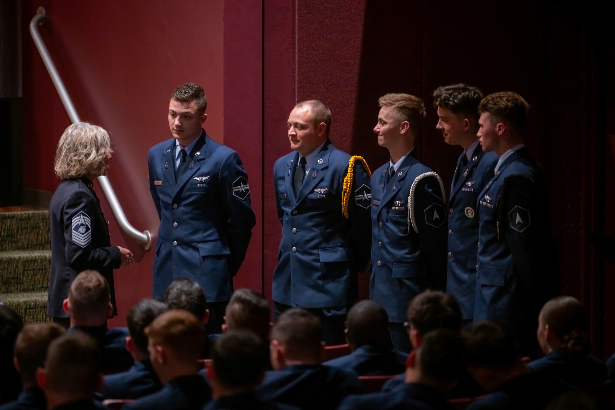 Military members in blue uniforms talk to one another in an auditorium.