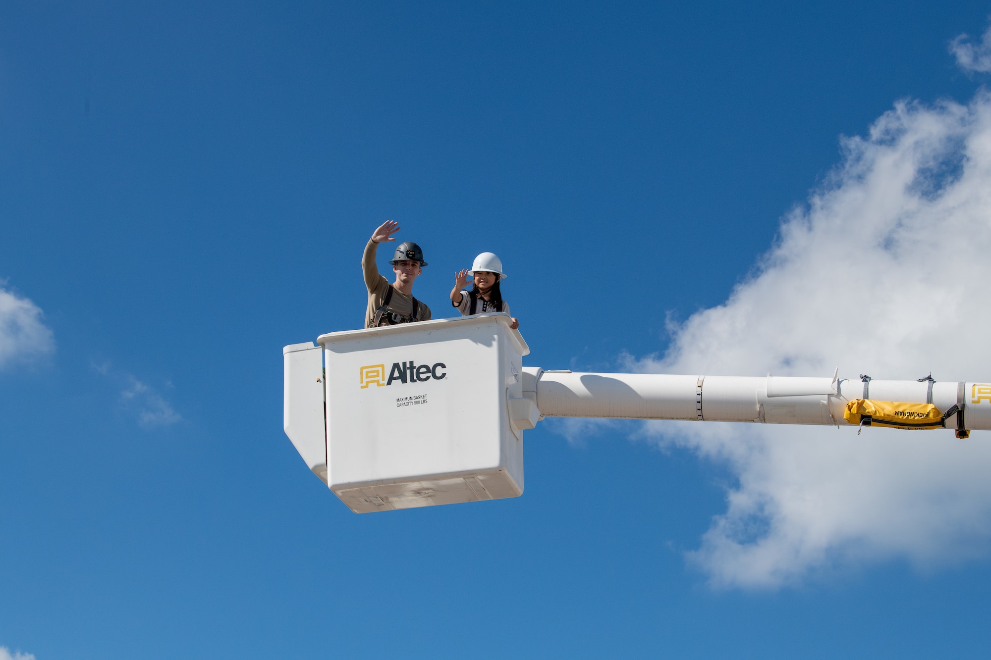 2 people wave while in a bucket truck