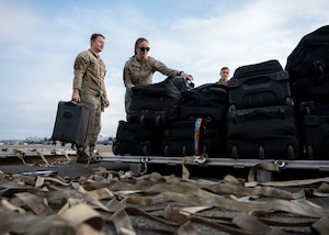 Military members pile luggage onto a pallet.