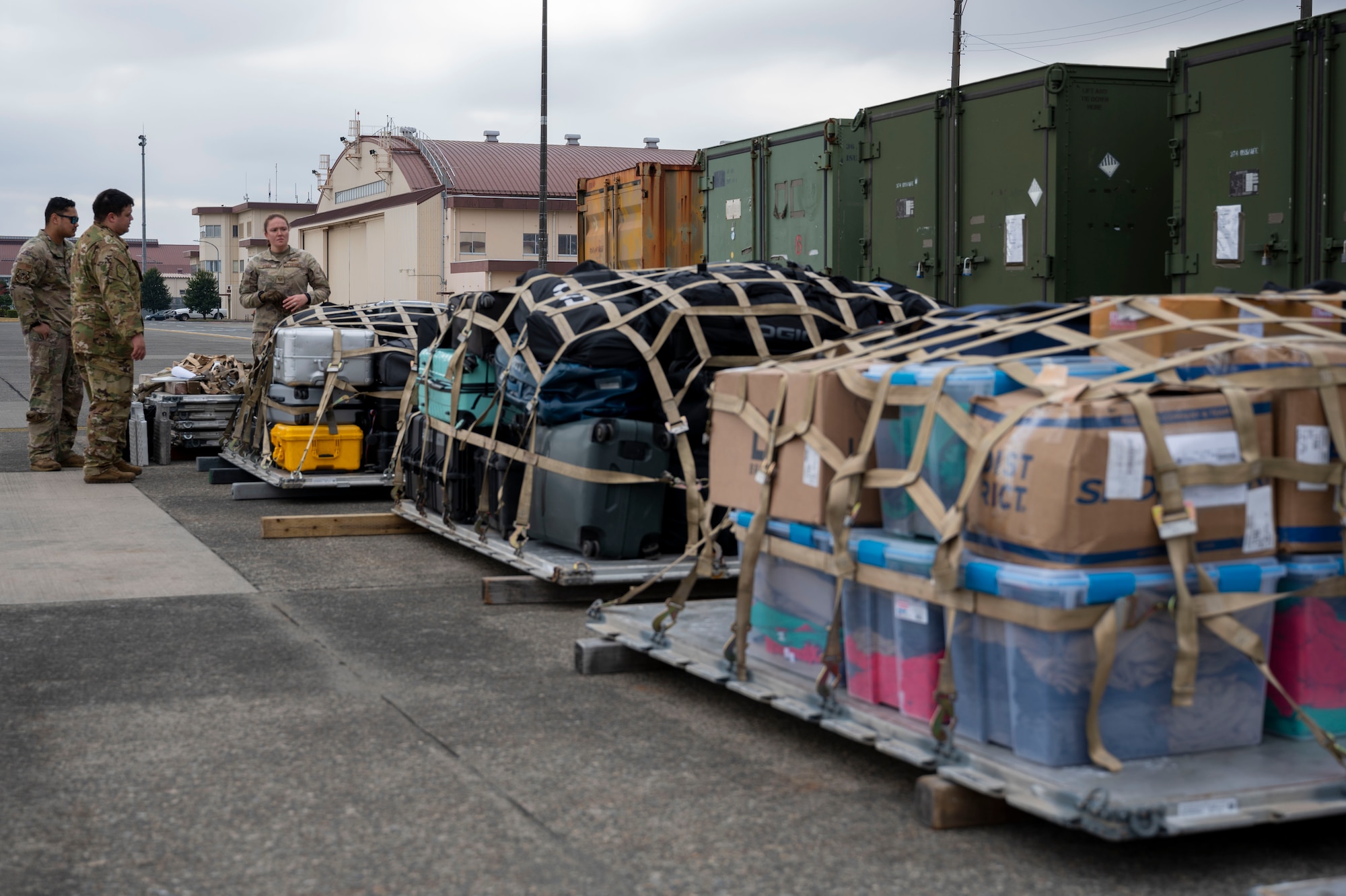 Three military members inspect three pallets of luggage.
