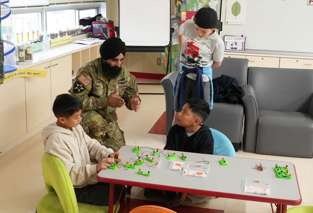 Lt. Col. Simratpal “Simmer” Singh, Deputy Commander of the U.S. Army Corps of Engineers Japan District (USACE JED), instructs students from Naval Air Facility Atsugi’s Shirley Lanham Elementary School on how to build an electrical circuit during the school’s annual Science Technology Engineering Art and Mathematics (STEAM) Day event, December 3rd, 2025. Singh brought specialized children’s electrical circuit-building kits equipped with snap-on wires, safe low-voltage batteries, switches, and small lightbulbs. These kits allowed students to construct working circuits without soldering or tools, helping them understand how electricity flows and how components interact within a system. Photo by Patrick Ciccarone.