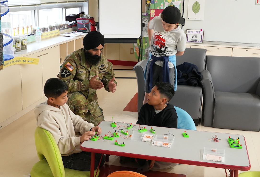 Lt. Col. Simratpal “Simmer” Singh, Deputy Commander of the U.S. Army Corps of Engineers Japan District (USACE JED), instructs students from Naval Air Facility Atsugi’s Shirley Lanham Elementary School on how to build an electrical circuit during the school’s annual Science Technology Engineering Art and Mathematics (STEAM) Day event, December 3rd, 2025. Singh brought specialized children’s electrical circuit-building kits equipped with snap-on wires, safe low-voltage batteries, switches, and small lightbulbs. These kits allowed students to construct working circuits without soldering or tools, helping them understand how electricity flows and how components interact within a system. Photo by Patrick Ciccarone.