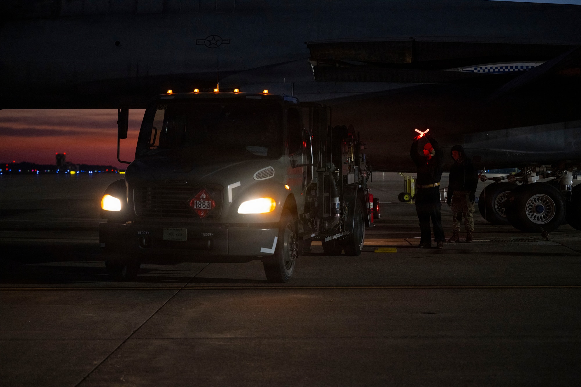 U.S. Air Force Senior Airman Henry Uriarte, 9th Expeditionary Bomb Squadron crew chief, marshals a fuel truck to hot pit refuel a B-1B Lancer before its return to Dyess Air Force Base, Texas, at Misawa Air Base, Japan, Nov. 17, 2025. Hot pit refueling leads to faster and more agile operations  by allowing the aircraft to refuel without stopping their engines. (U.S. Air Force photo by Senior Airman Emma Anderson)