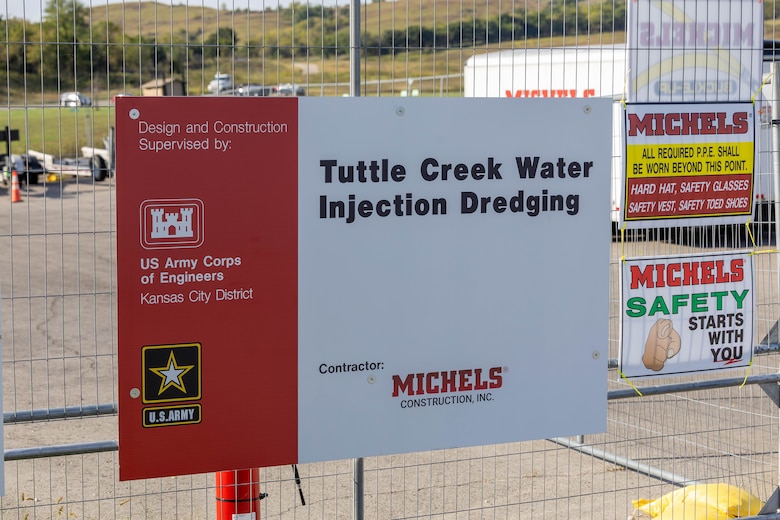 A red and white poster with black and white text hangs on a chain link fence.