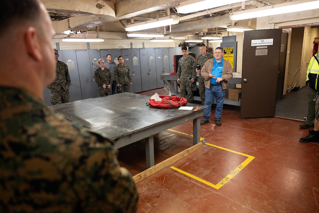 Robert Hazlett, contracting officer's technical representative for Blount Island Command, explains a tool and maintenance room aboard the USNS Sgt. William R. Button during a visit by a Marine Expeditionary Force liaison team on Dec. 2, 2025, at Marine Corps Support Facility Blount Island, Florida. Hazlett, a Marine Corps veteran who served six years in motor transportation and nearly 20 years afloat as a KBR contractor—including six years as a squadron supervisor— became a sworn civilian at Blount Island in 2024. (Official Marine Corps Photo by Dustin Senger)