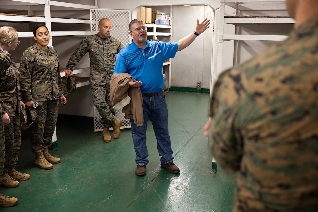Robert Hazlett, contracting officer's technical representative for Blount Island Command, explains a battery storage room aboard the USNS Sgt. William R. Button during a visit by a Marine Expeditionary Force liaison team on Dec. 2, 2025, at Marine Corps Support Facility Blount Island, Florida. Hazlett, a Marine Corps veteran who served six years in motor transportation and nearly 20 years afloat as a KBR contractor—including six years as a squadron supervisor— became a sworn civilian at Blount Island in 2024. (Official Marine Corps Photo by Dustin Senger)