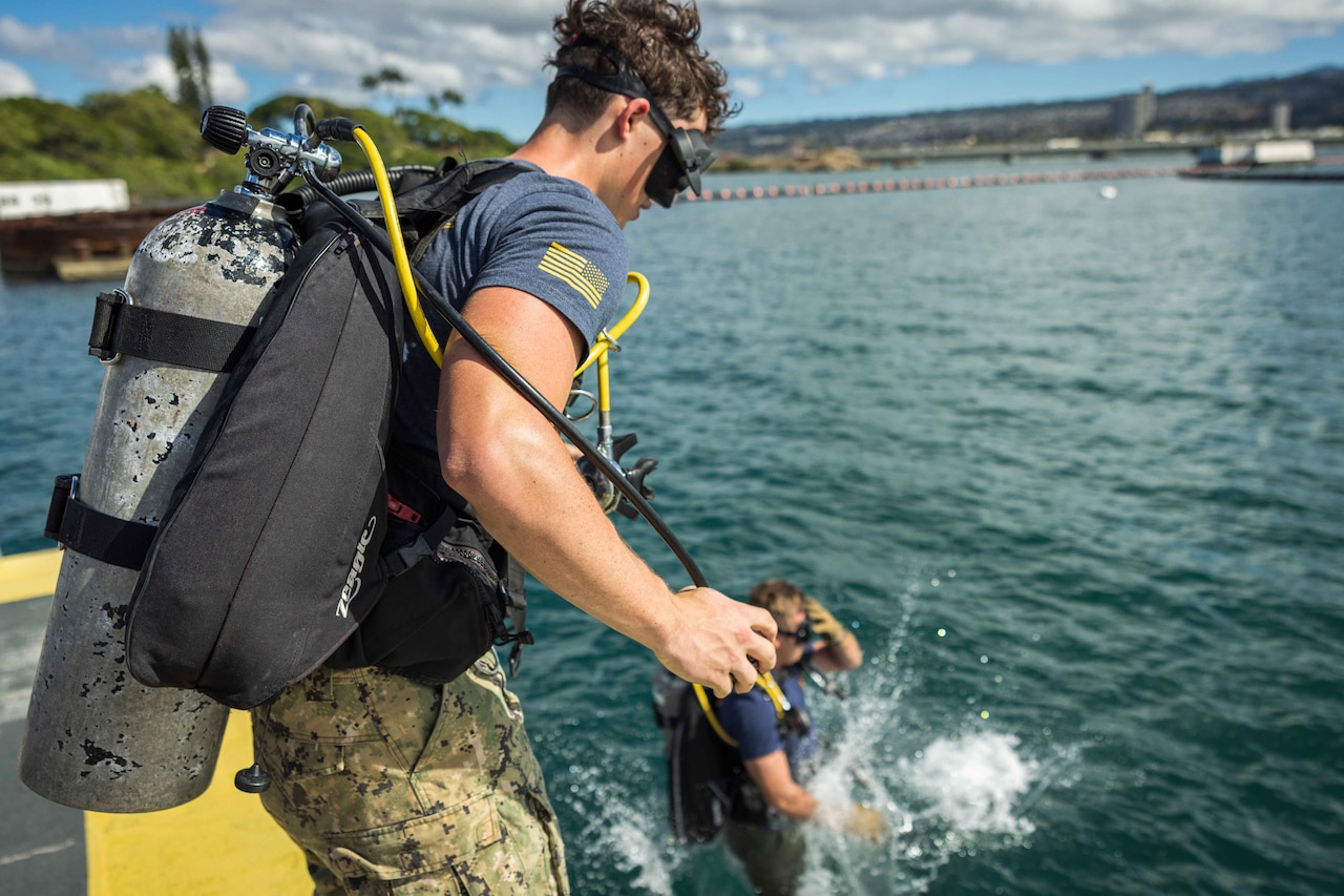 Two people in scuba-diving equipment jump into the water.
