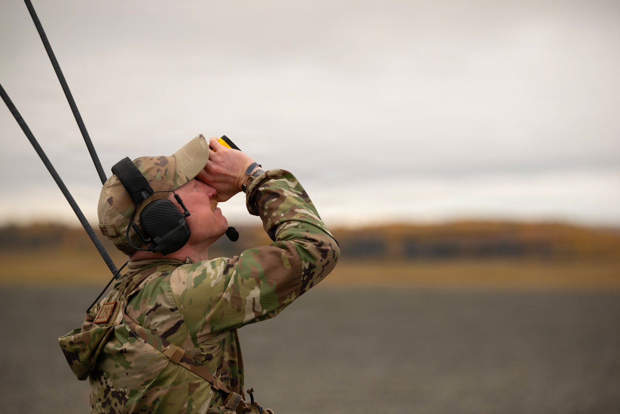 Tech. Sgt. Dylan Drenner, a landing zone safety officer (LZSO) assigned to the 3rd Operations Support Squadron, uses a rangefinder to assess a landing during an austere-environment landing exercise on Joint Base Elmendorf-Richardson, Alaska, Sept. 26, 2025. LZSOs practice management of landing zones, airspace management and coordination for medical evacuation personnel. Checking for streamlined communication with all personnel on the flightline ensures safety and readiness among all personnel on the flightline. (U.S. Air Force photo by Airman Vischi)