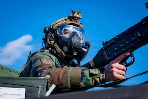 A cop in a gas mask looks right while indexing a machine gun