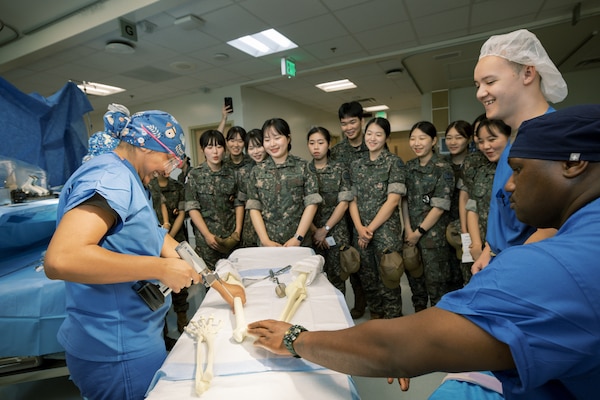 Hospital Corpsman 3rd Class Victoria Moralez, left, demonstrates the use of a reciprocating bone saw on a training model for Republic of Korea (ROK) Military Nursing Academy cadets during a surgical skills station at U.S. Naval Hospital Guam, Nov. 14, 2025. Lt. Terrance Cheatham, second from right, a U.S. Navy perioperative nurse, and Hospitalman Tru Yang, right, assisted the demonstration, providing the cadets hands-on exposure to simulated operative procedures. (U.S. Navy photo by Hospital Corpsman 1st Class Clien Lester Guico.)