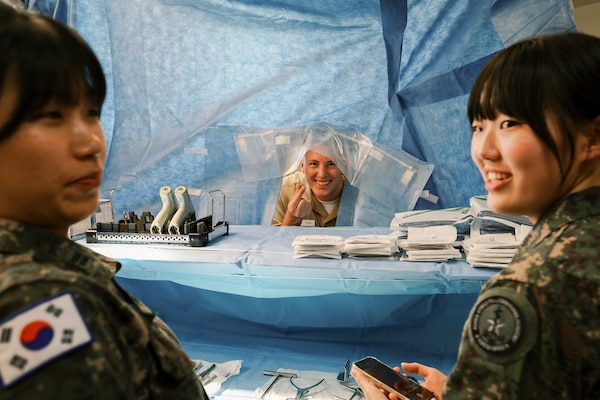 Lt. Cmdr. Ian Ryan interacts with Republic of Korea (ROK) Military Nursing Academy cadets using a surgical backdrop during a simulated operating room tour at U.S. Naval Hospital Guam, Nov. 14, 2025. The demonstration was part of an immersive series of skills stations highlighting operating room procedures and surgical workflow for visiting cadets. (U.S. Navy photo by Hospital Corpsman 1st Class Clien Lester Guico.)
