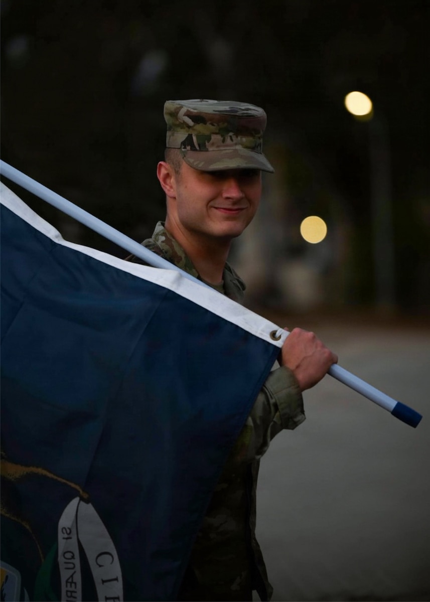 a us airman poses with a blue flag over his shoulder, beige bokeh nit he back from lights
