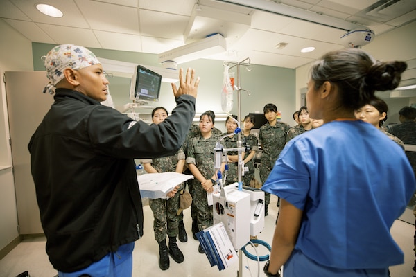 Lt. Joseph Roberto and Lt. Angelica Bustamante demonstrate the setup and use of a rapid infuser system for Republic of Korea (ROK) Military Nursing Academy cadets during a clinical skills rotation at U.S. Naval Hospital Guam, Nov. 14, 2025. The hands-on station introduced cadets to resuscitation equipment and emergency workflow utilized in surgical and critical care environments. (U.S. Navy photo by Hospital Corpsman 1st Class Clien Lester Guico.)