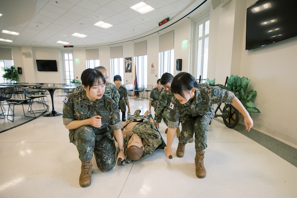 Republic of Korea (ROK) Military Nursing Academy cadets practice patient movement techniques using a stretcher during a hands-on skills station at U.S. Naval Hospital Guam, Nov. 14, 2025. The scenario-based rotation introduced cadets to fundamentals of casualty transport and teamwork used in clinical and operational medical environments. (U.S. Navy photo by Hospital Corpsman 1st Class Clien Lester Guico.)