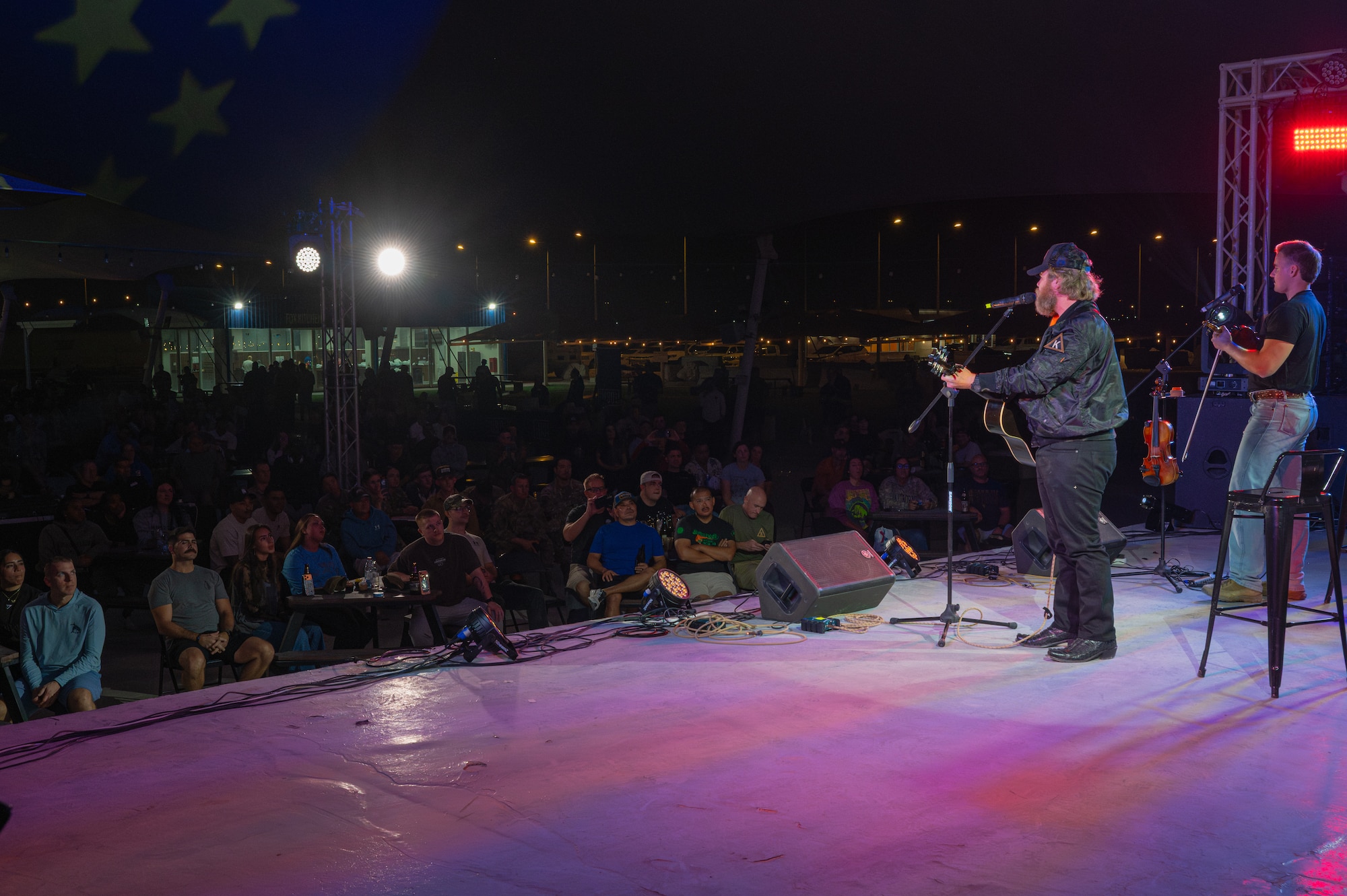 A man sings and plays guitar onstage while beyond, a crowd of people listening