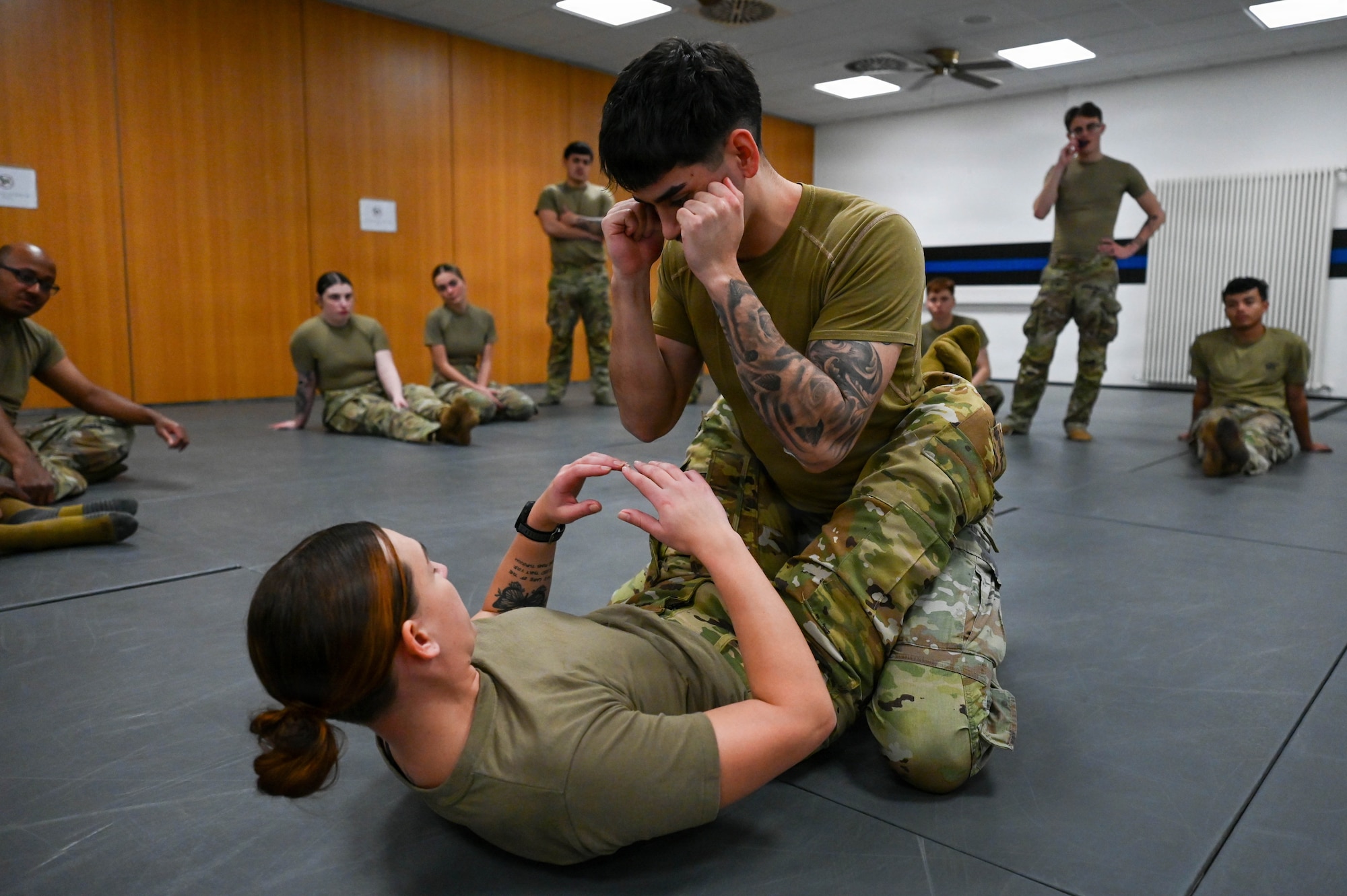 U.S. Air Force Staff Sgt. Kristen Wurtz, bottom, 446th Security Forces Squadron Phoenix Raven team member, and Senior Airman Alexandro Ochoa, 86th Security Forces training instructor, demonstrate combative maneuvers to in-processing 86th Security Forces Airmen at Ramstein Air Base, Germany, Nov. 24, 2025.