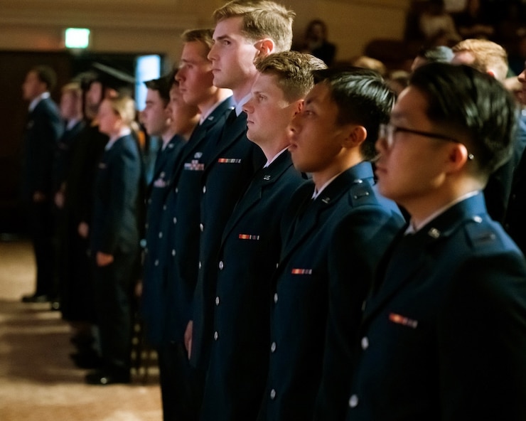 U.S. Airmen in uniform stand in line as they participate in a graduation ceremony celebrating their accomplishments in support of the United States Air Force and their own military careers.