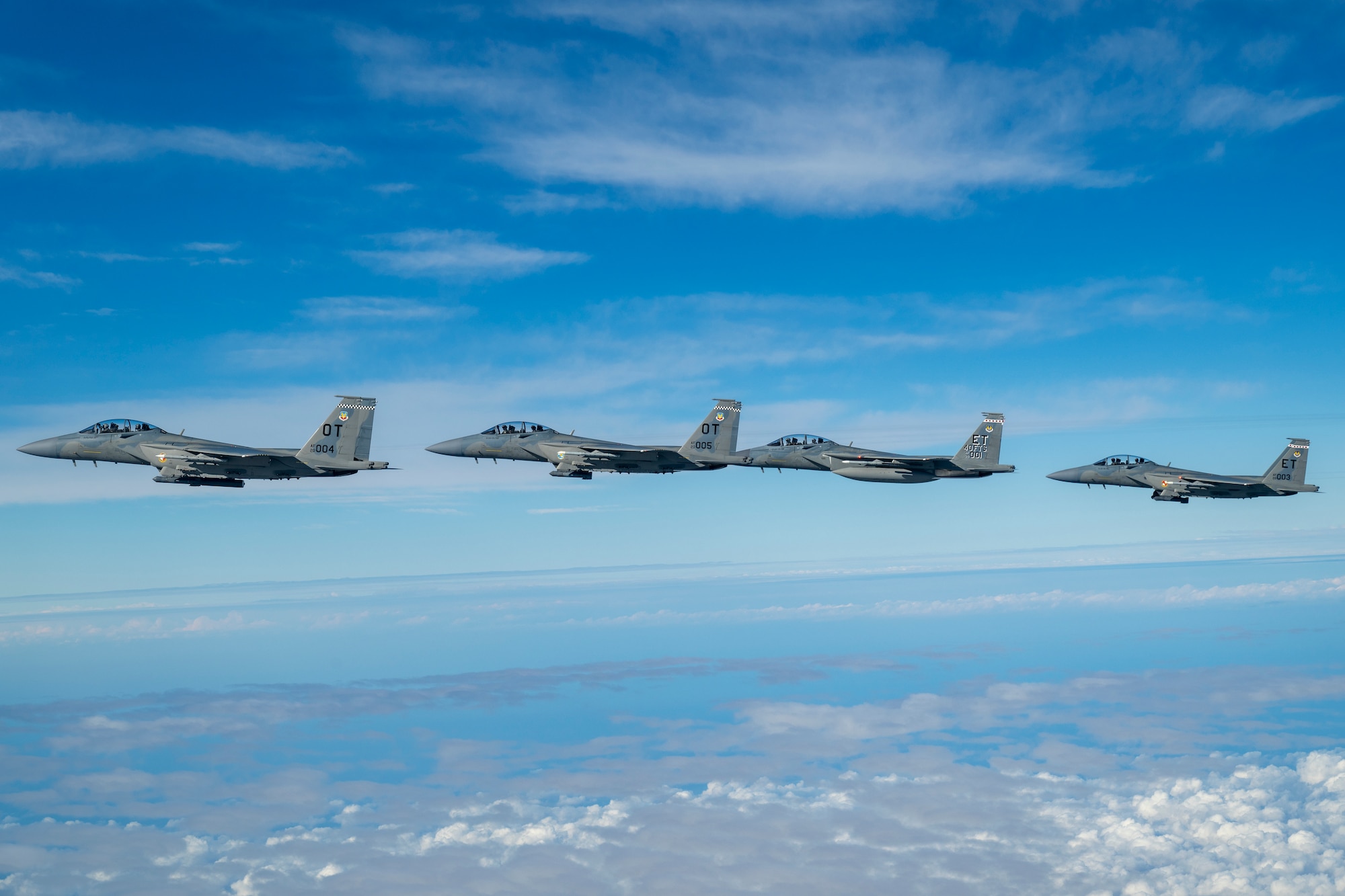 F-15 flying in formation of 4 planes. Sky is blue with lots of clouds. 