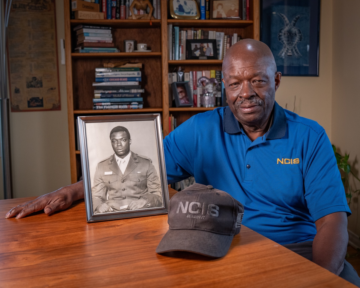 Leon Carroll, Jr. poses with a photo of him when he was a Marine and an NCIS baseball cap at his home in Long Beach, California.