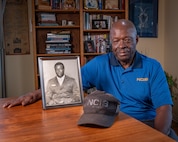 Leon Carroll, Jr. poses with a photo of him when he was a Marine and an NCIS baseball cap at his home in Long Beach, California.