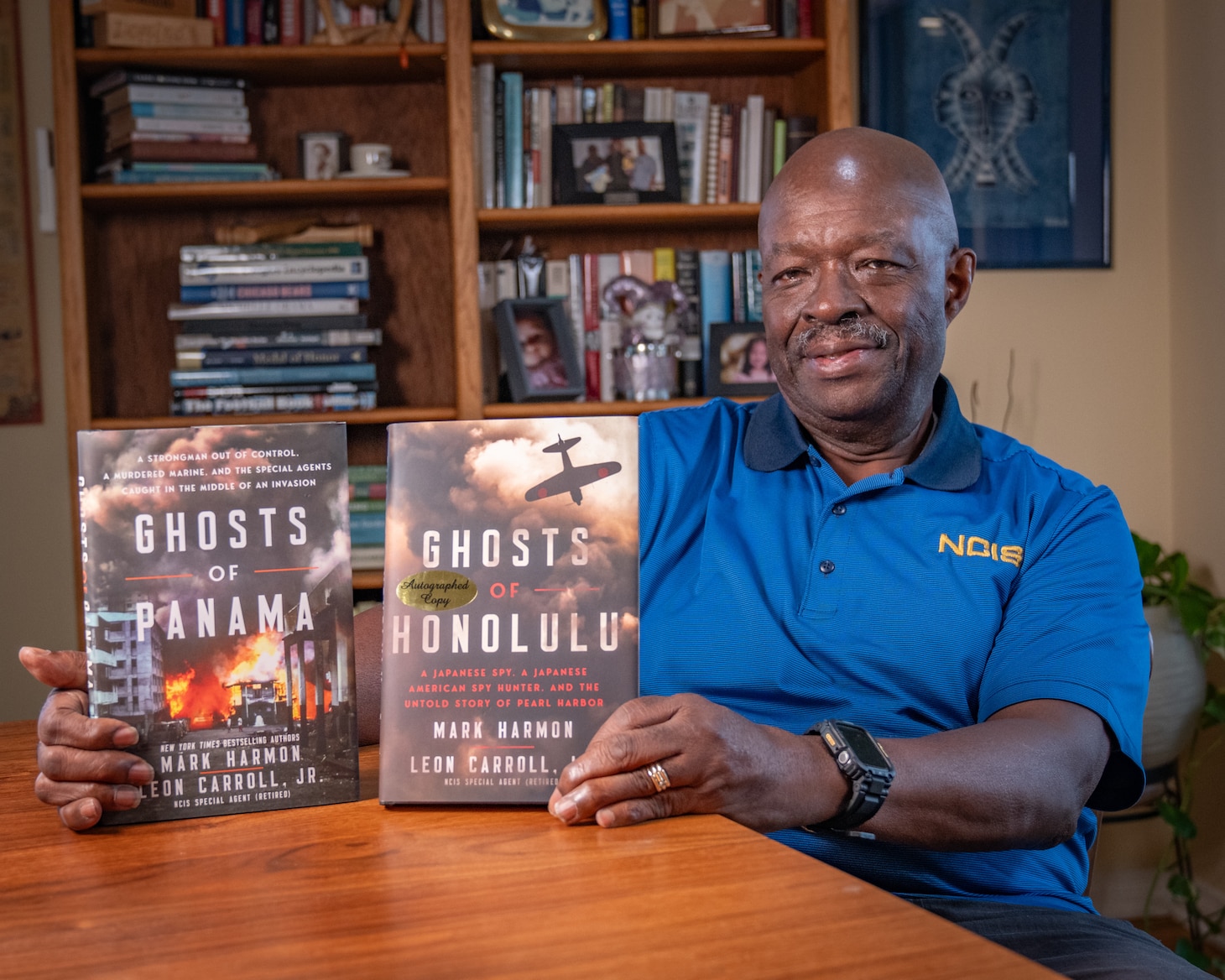 Retired NCIS Special Agent Leon Carroll sits at a table in his home and shows off the two books with co-wrote with actor Mark Harmon.