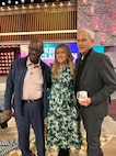 Retired Special Agent Leon Carroll on the left, singer and talk show host Kelly Clarkson in the middle, and actor Mark Harmon on the right stand together on the set of the Kelly Clarkson show.