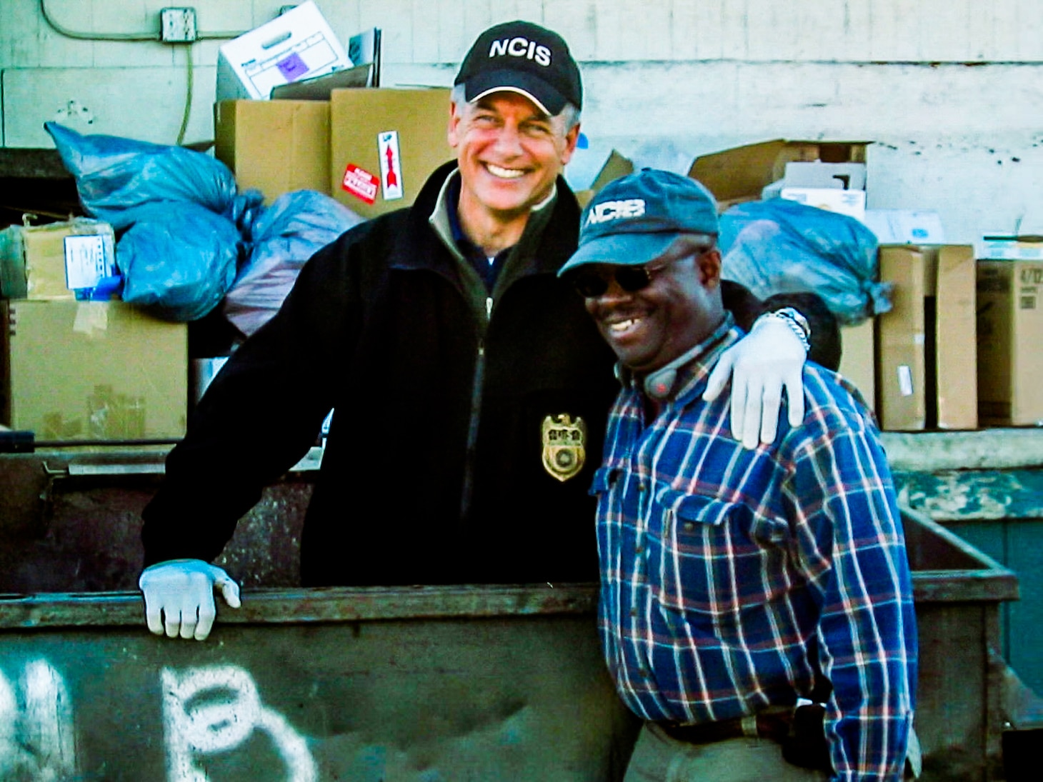 Actor Mark Harmon standing in a garbage dumpster with former-NCIS Special Agent Leon Carroll standing next to him outside the dumpster.