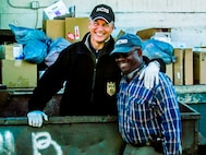 Actor Mark Harmon standing in a garbage dumpster with former-NCIS Special Agent Leon Carroll standing next to him outside the dumpster.