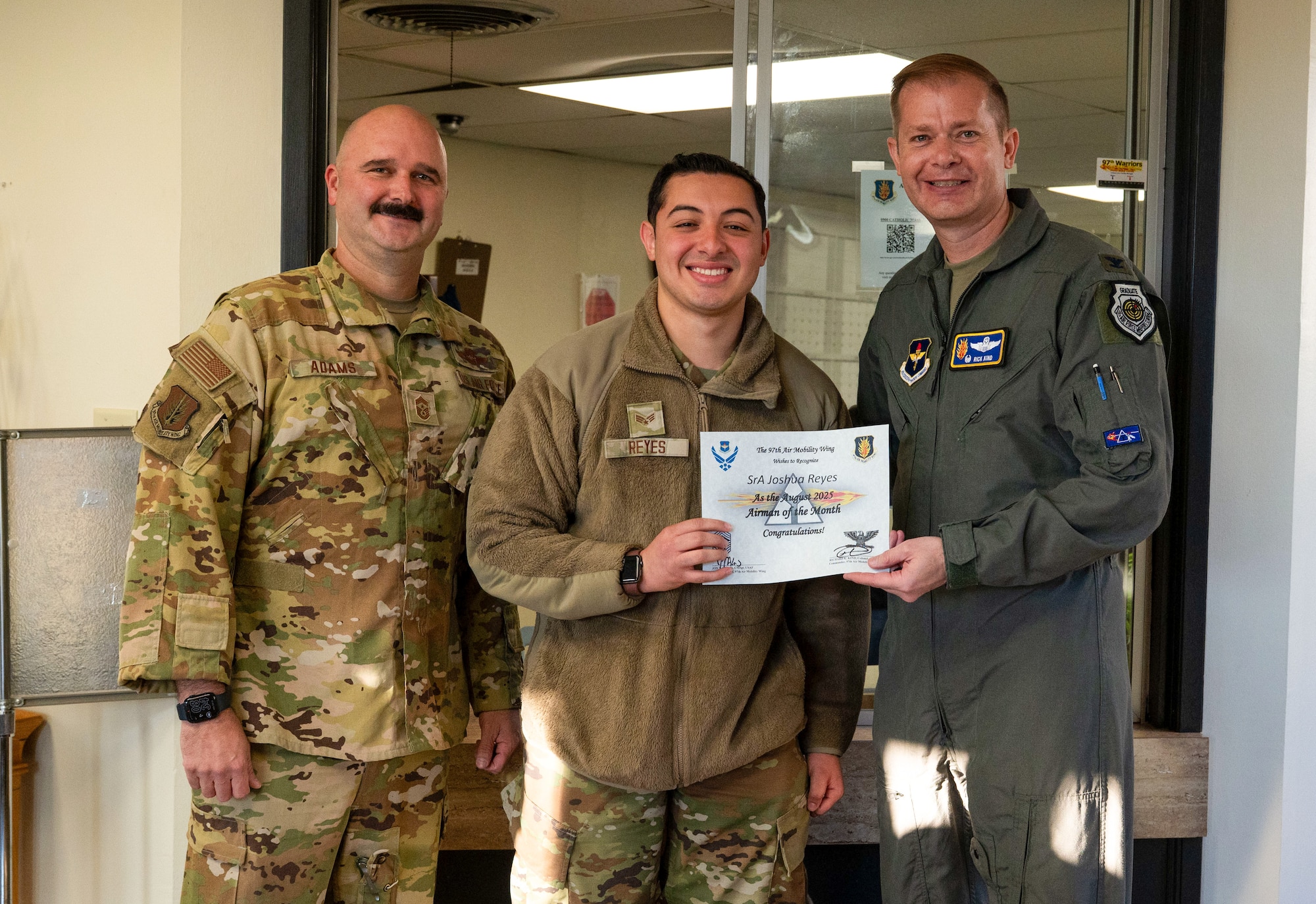 U.S. Air Force Col. Richard Kind, right, 97th Air Mobility Wing (AMW) commander , and Chief Master Sgt. Jonny Adams, left, 97th AMW command chief, hands an award to Senior Airman Joshua Reyes, center, 97th AMW Chapel Office religious affairs airman, at Altus Air Force Base, Oklahoma, Sept. 29, 2025. Reyes was named the Airman of the Month for August 2025. (U.S. Air Force photo by Tech. Sgt. Hailey Haux)