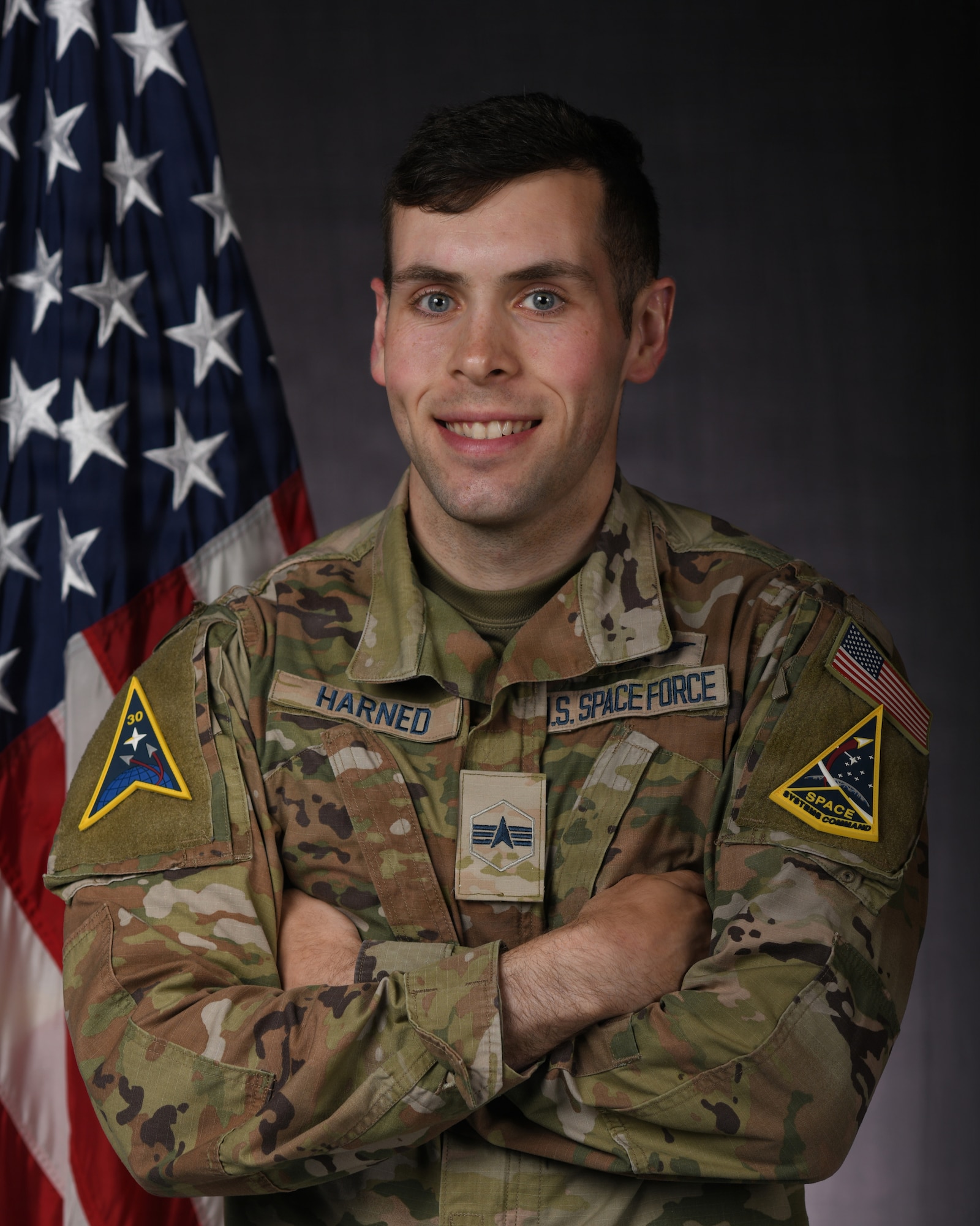 a person in military uniform poses next to a us flag and smiles for a photo